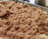 Photo of apple crisp before baking with apples at the bottom of a glass pan and crumbs on top