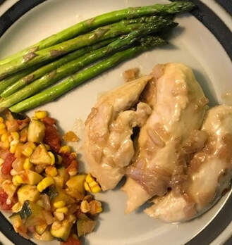 Chicken with onion sauce on a plate with asparagus and mixed vegetables